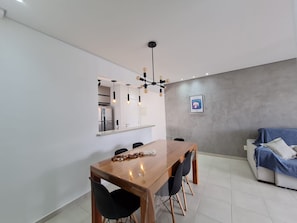 Ein stilvoller Essbereich mit Holztisch und schwarzen Stühlen, im Hintergrund eine Küche und eine graue Wand mit einem gerahmten Bild.