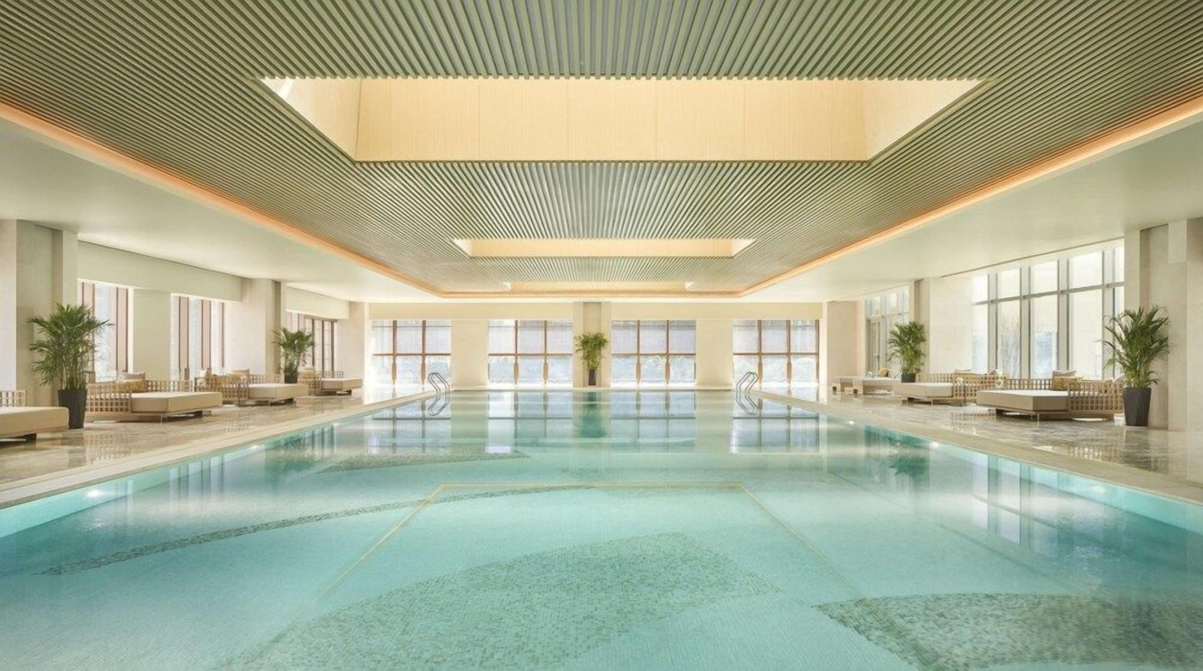 A large indoor swimming pool with a modern design, surrounded by seating areas and large windows.