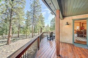 A wooden deck with a view of a forest, a seating area with chairs, and a building entrance. - Ruby Mountain House With EV Charger (Buena Vista)