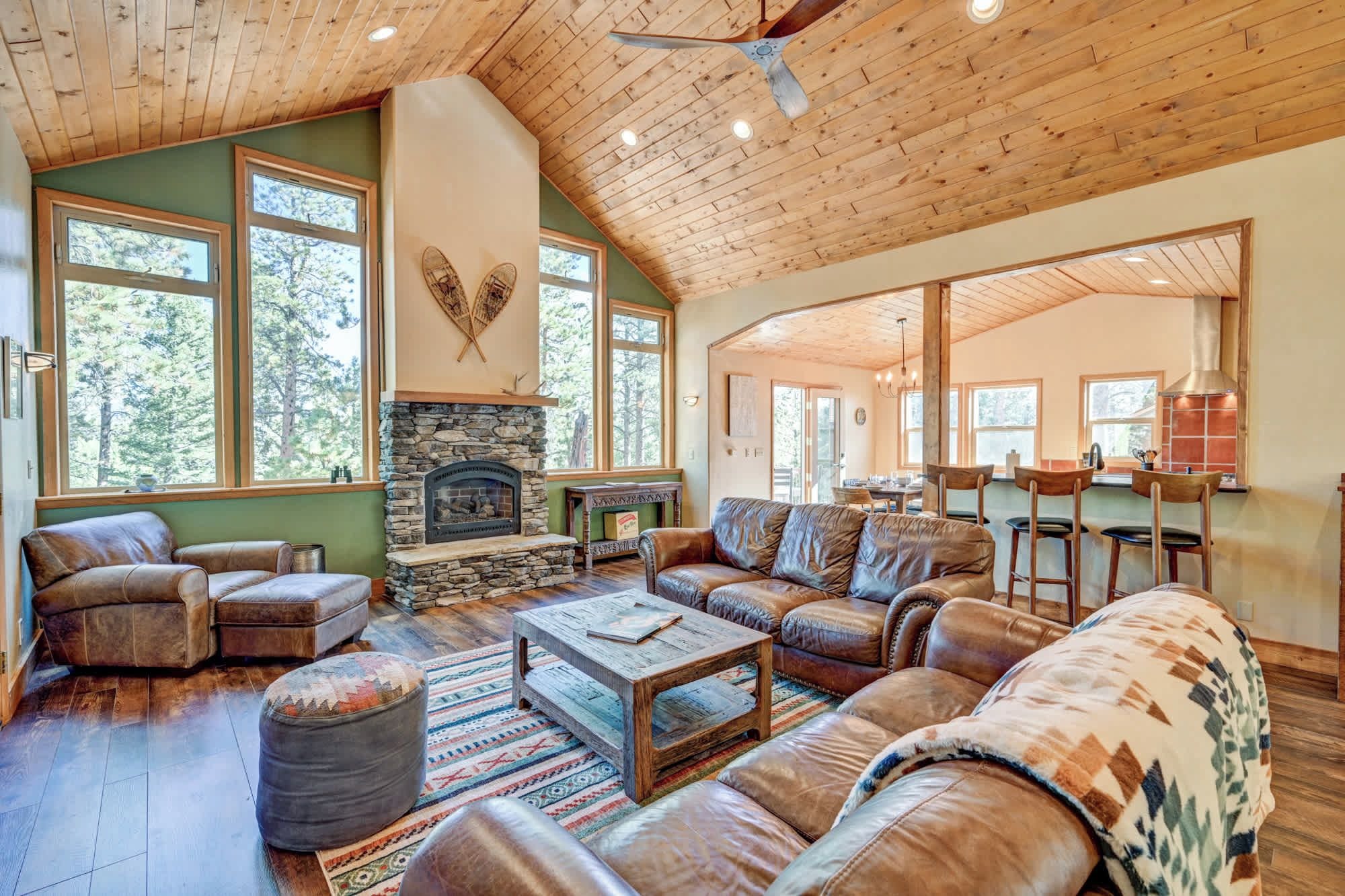 A spacious living room with a stone fireplace, leather sofas, and a large window overlooking a forest.