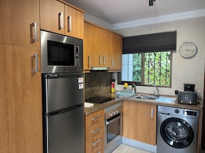 Una cocina moderna con electrodomésticos de acero inoxidable, armarios de madera, horno empotrado y lavadora.