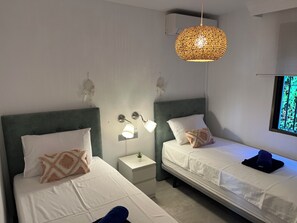 Ein Hotelzimmer mit zwei Einzelbetten, einem Nachttisch mit Lampe, einer Wandleuchte und einem Fenster mit Blick.