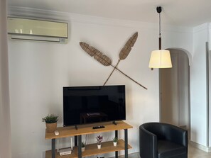 A modern living room with a flat-screen TV on a wooden stand, a black leather chair, a wall-mounted air conditioner, and a decorative wall art piece. - Family Garden Retreat-Las Farolas-Mijas Costa (AN)