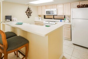 A kitchen with a central island, white cabinets, a microwave, a stove, and a refrigerator. - Beachfront 1BR Condo w/ Balcony View + King Bed (South Padre Island)