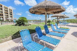 A resort with outdoor lounge chairs, thatched umbrellas, and a pool area. - Beachfront 1BR Condo w/ Balcony View + King Bed (South Padre Island)