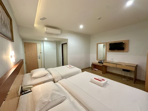 A hotel room with two beds, a desk, a TV, and an air conditioning unit. - Aquatel Hotel (Pekanbaru)