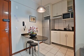 Eine kompakte Küche mit Kühlschrank, Mikrowelle und einer kleinen Essecke mit Hocker.