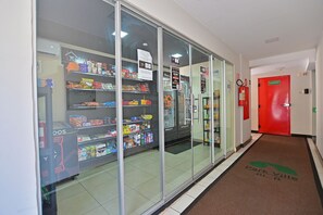 Ein Korridor mit einem Getränkeautomaten, der mit Snacks und Getränken gefüllt ist, einem an der Wand befestigten Feuerlöscher und einer roten Tür am Ende.