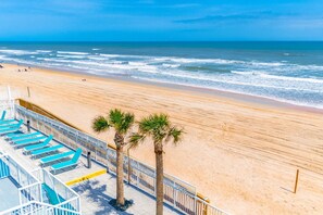 A beach with a pool area, palm trees, and a clear view of the ocean. - ADA Oceanfront Studio | Games, Pool & Picnic Area (Ormond Beach)