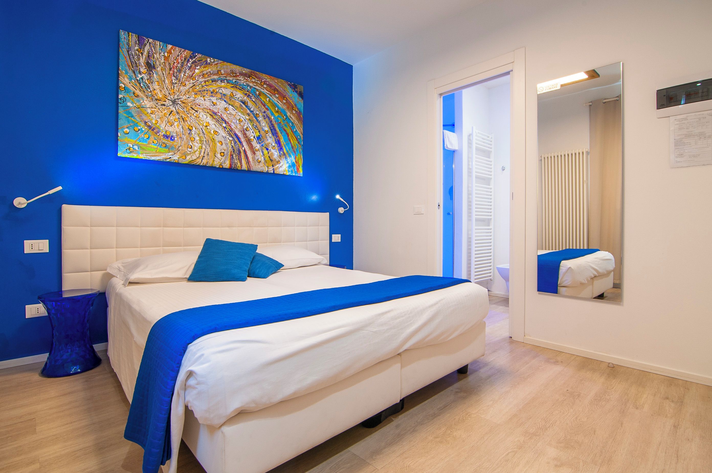 Una camera da letto con un letto grande, una parete azzurra e un quadro astratto colorato.