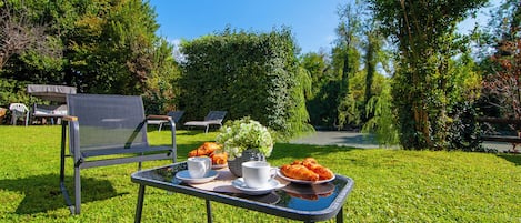 Un área de estar al aire libre con una mesa lista para comer, sillas y vistas a un jardín.