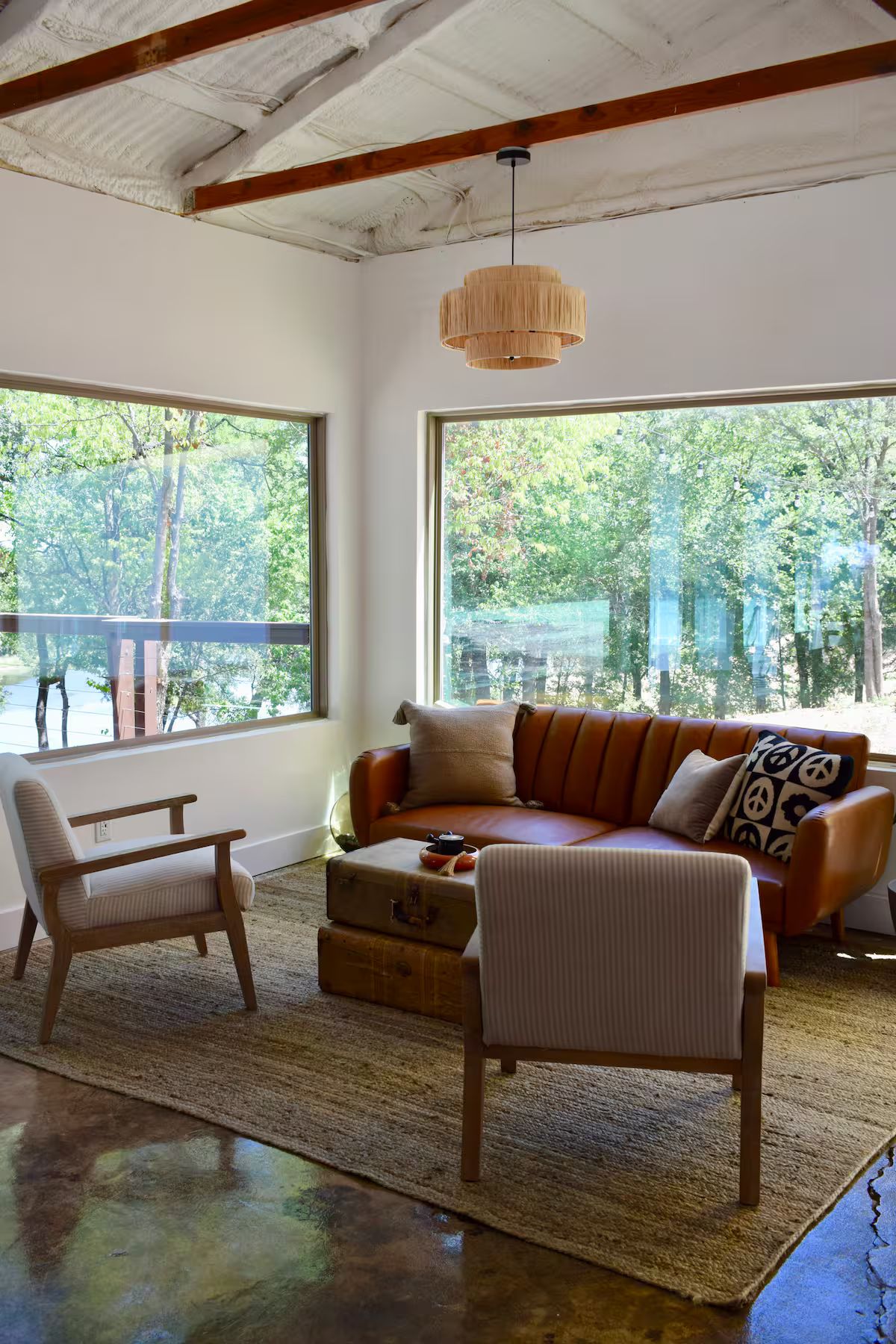 A modern living room with a large window, a sofa, two chairs, and a hanging light fixture.