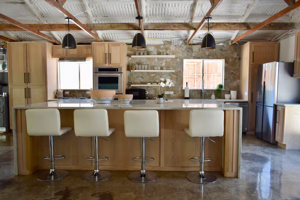 Een keuken met een centraal eiland, barkrukken en moderne apparatuur.