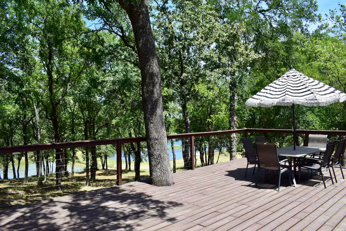 Una terraza de madera con una mesa y sillas, rodeada de árboles y con vistas a un cuerpo de agua.