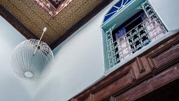 A room with a patterned ceiling, a hanging light fixture, and a window with a decorative grille.