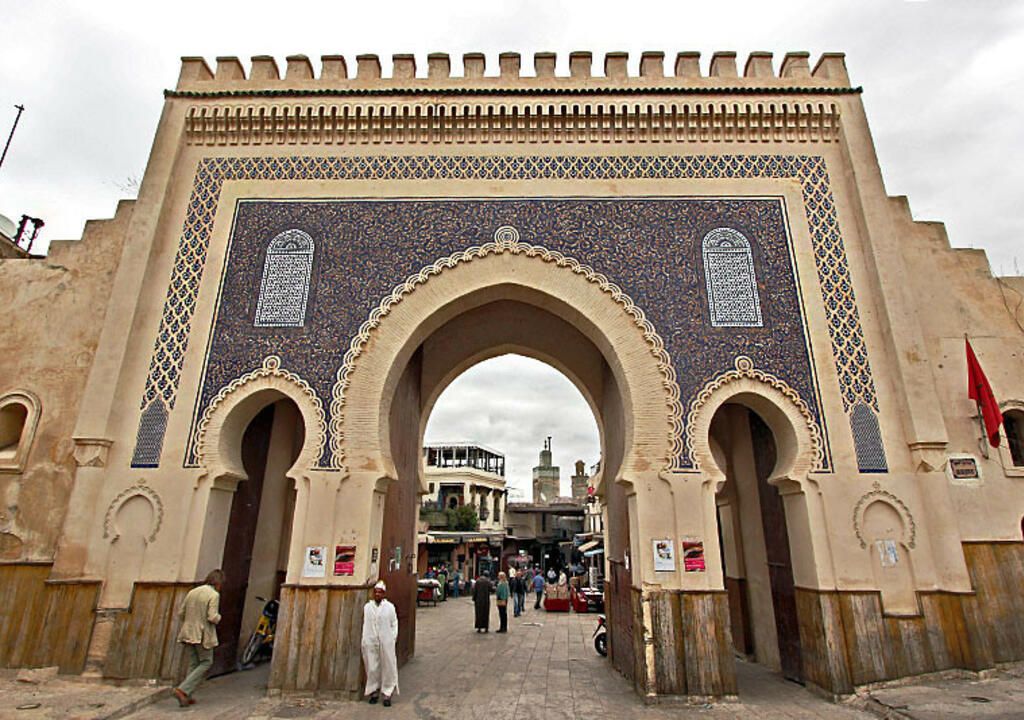 A large archway with intricate tile work and a flag on the right.