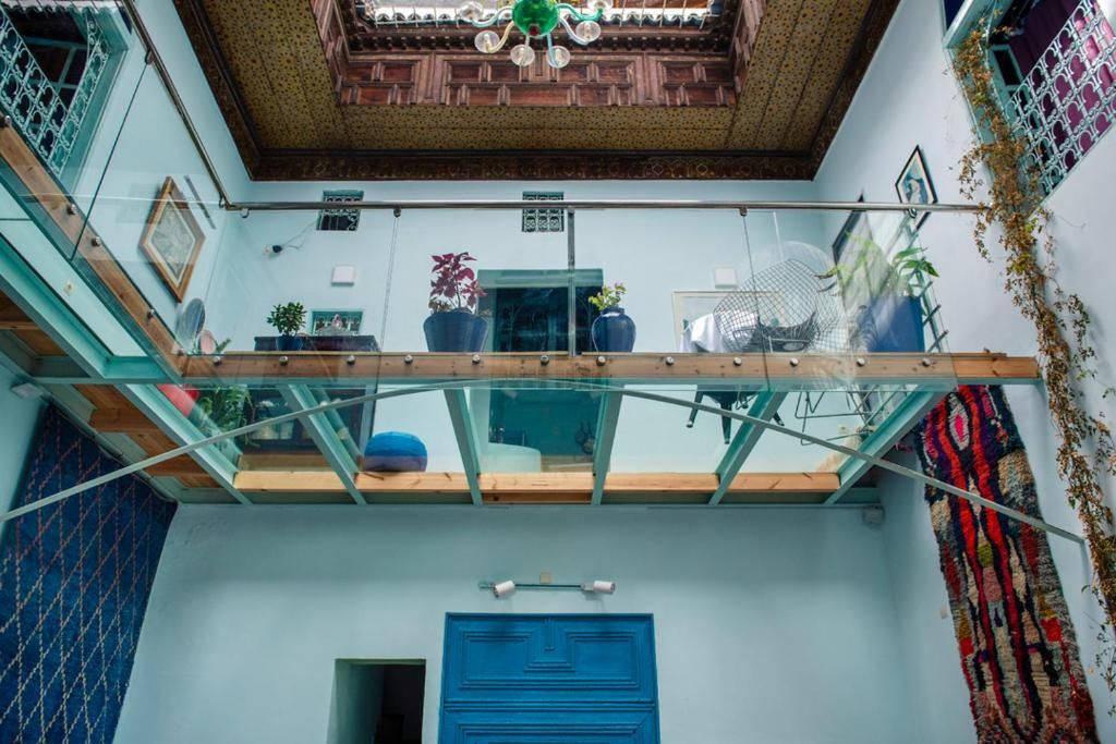 A multi-level interior with a glass balcony, a blue door, and potted plants.