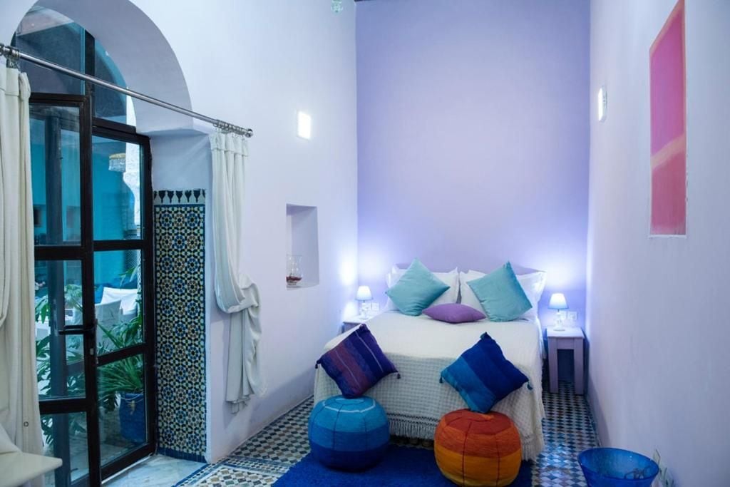 A narrow hotel room with a bed, two bedside lamps, a window with curtains, and a small balcony.