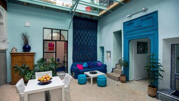 A cozy courtyard with a blue sofa, a dining table with fruit, and potted plants.