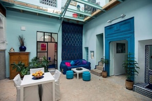 A cozy courtyard with a blue sofa, a dining table with fruit, and potted plants. - Dar Anne – Traditional Guesthouse in Fez (Fès)