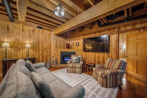 A cozy living room with a fireplace, a television, and a large window. - Mountain River Retreat | Fire Pit, Kayaks & Golf (Mentone)