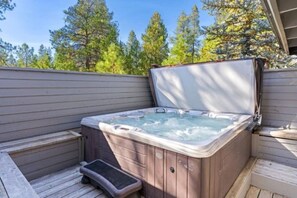 Ein Whirlpool auf einer Holzterrasse mit einer Holzverkleidung und Bäumen im Hintergrund.