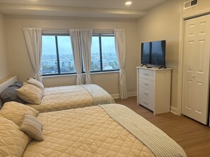 Un dormitorio con dos camas, un aparador, un televisor y vista a la ciudad desde la ventana.