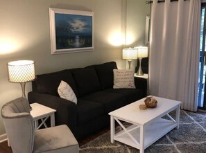 A living room with a black sofa, white side table, and a white coffee table. There is a framed picture on the wall and two lamps on either side of the sofa. - NEW Hilton Head Beach & Tennis Resort Building B Tennis Villa! (Hilton Head)