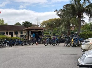 A parking area with multiple bicycles, a small building, and a palm tree. - NEW Hilton Head Beach & Tennis Resort Building B Tennis Villa! (Hilton Head)
