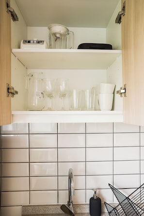 A kitchen with white cabinets, a tiled backsplash, a stainless steel sink, and various kitchen items like a kettle, glasses, and a coffee maker. - Sunny Studio in Nunoa for 3 Guests (Ñuñoa)