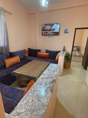A living room with a sofa, a coffee table, a TV mounted on the wall, and a Wi-Fi sign.