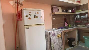 Cocina compacta con refrigerador, cilindro de gas, pileta y un estante con utensilios de cocina.