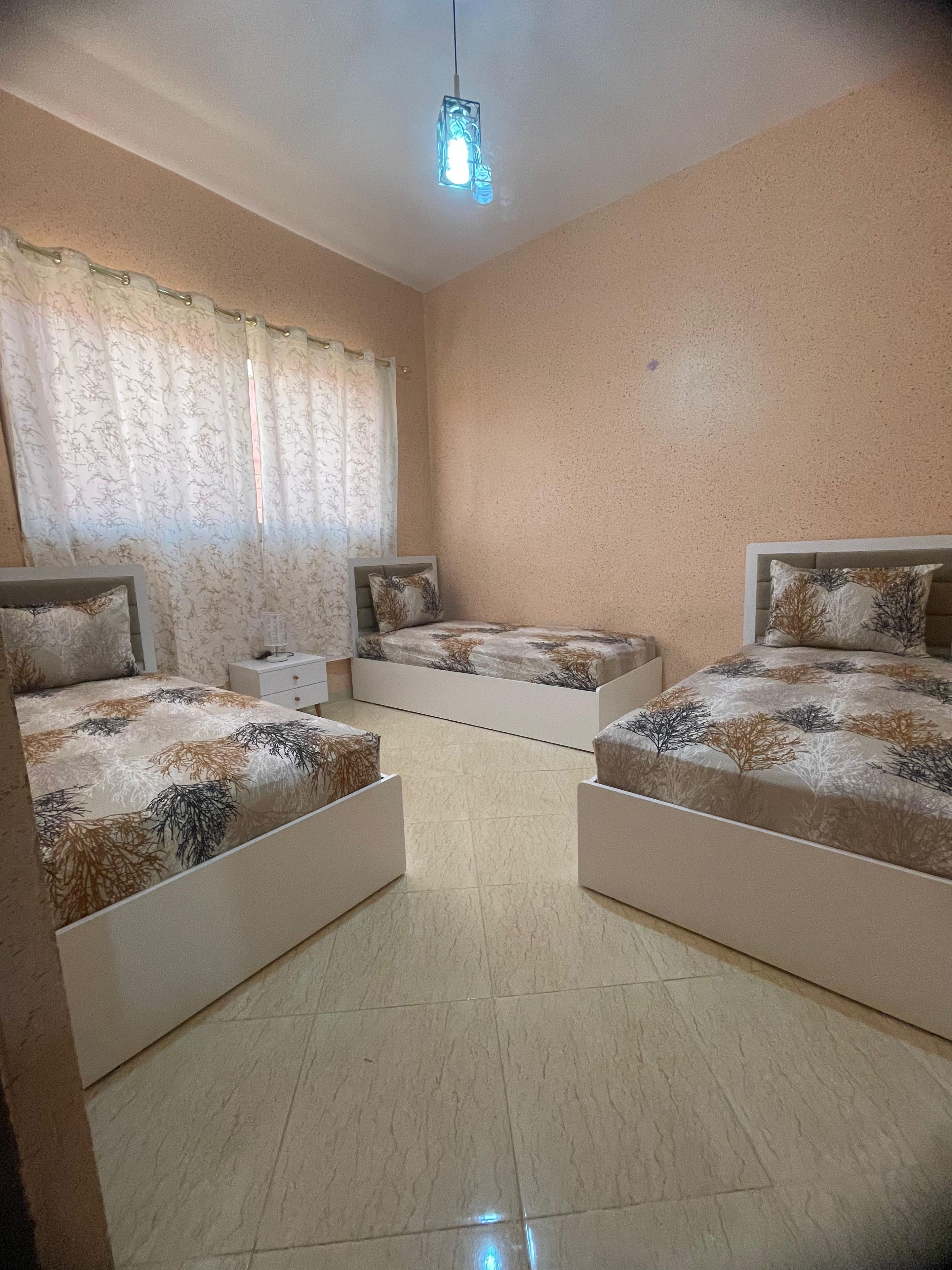 Ein Schlafzimmer mit zwei Betten, einem Nachttisch, einer Nachttischlampe und einer Pendelleuchte.