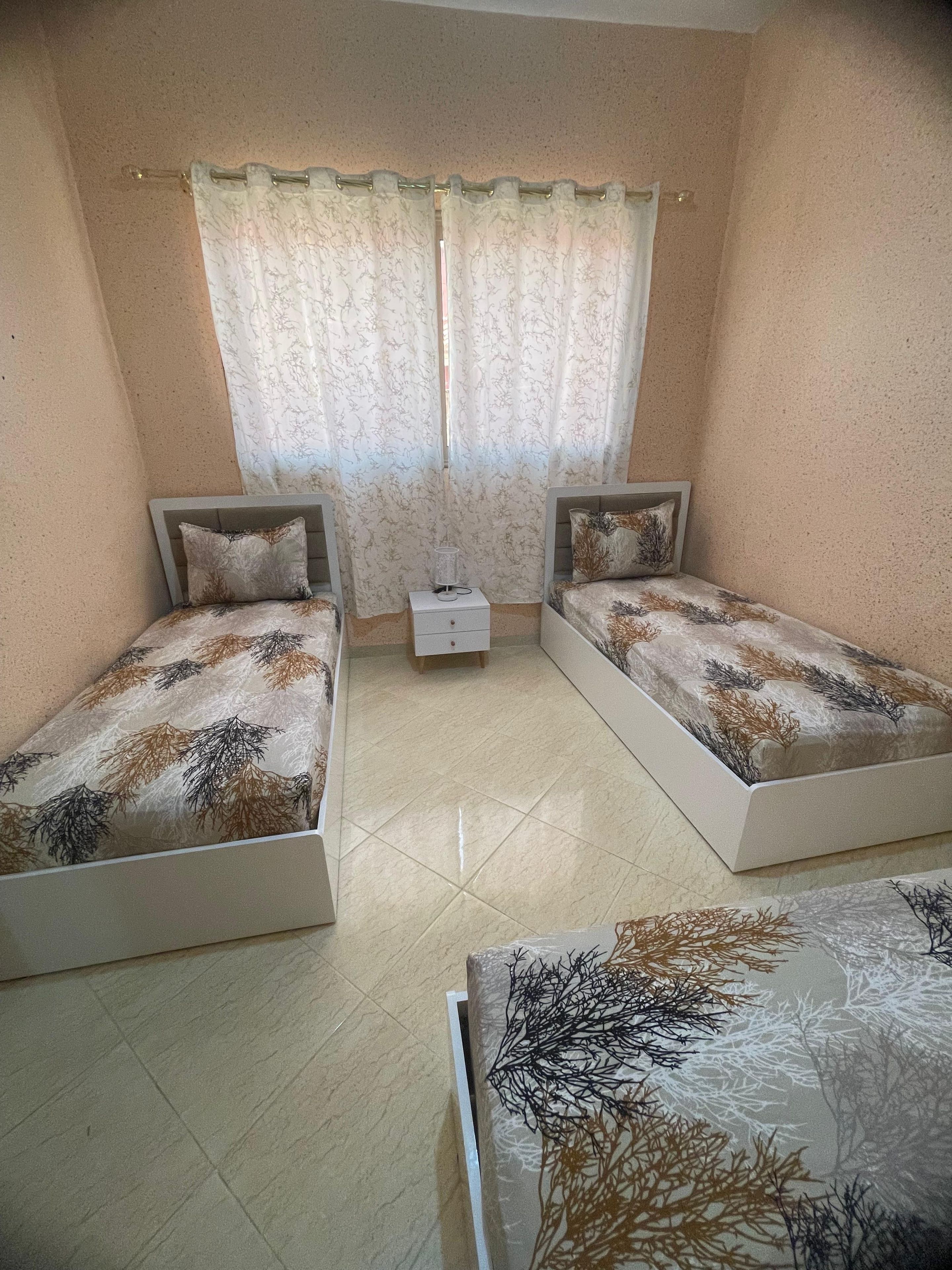Une chambre avec deux lits simples, une table de chevet et une fenêtre avec des rideaux.