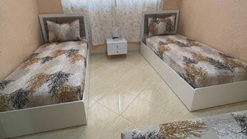 Une chambre avec deux lits simples, une table de chevet et une fenêtre avec des rideaux.