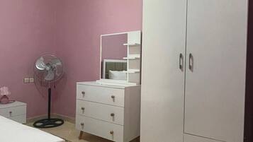 Un dormitorio con cama, cómoda, espejo, ventilador y armario.