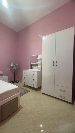 Un dormitorio con cama, cómoda, espejo, ventilador y armario.