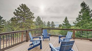 A deck with wooden flooring and a metal railing, surrounded by trees.
