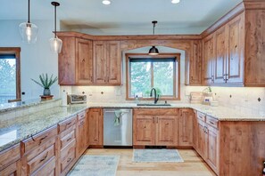 Una cocina con armarios de madera, encimeras de granito, lavavajillas e iluminación colgante.