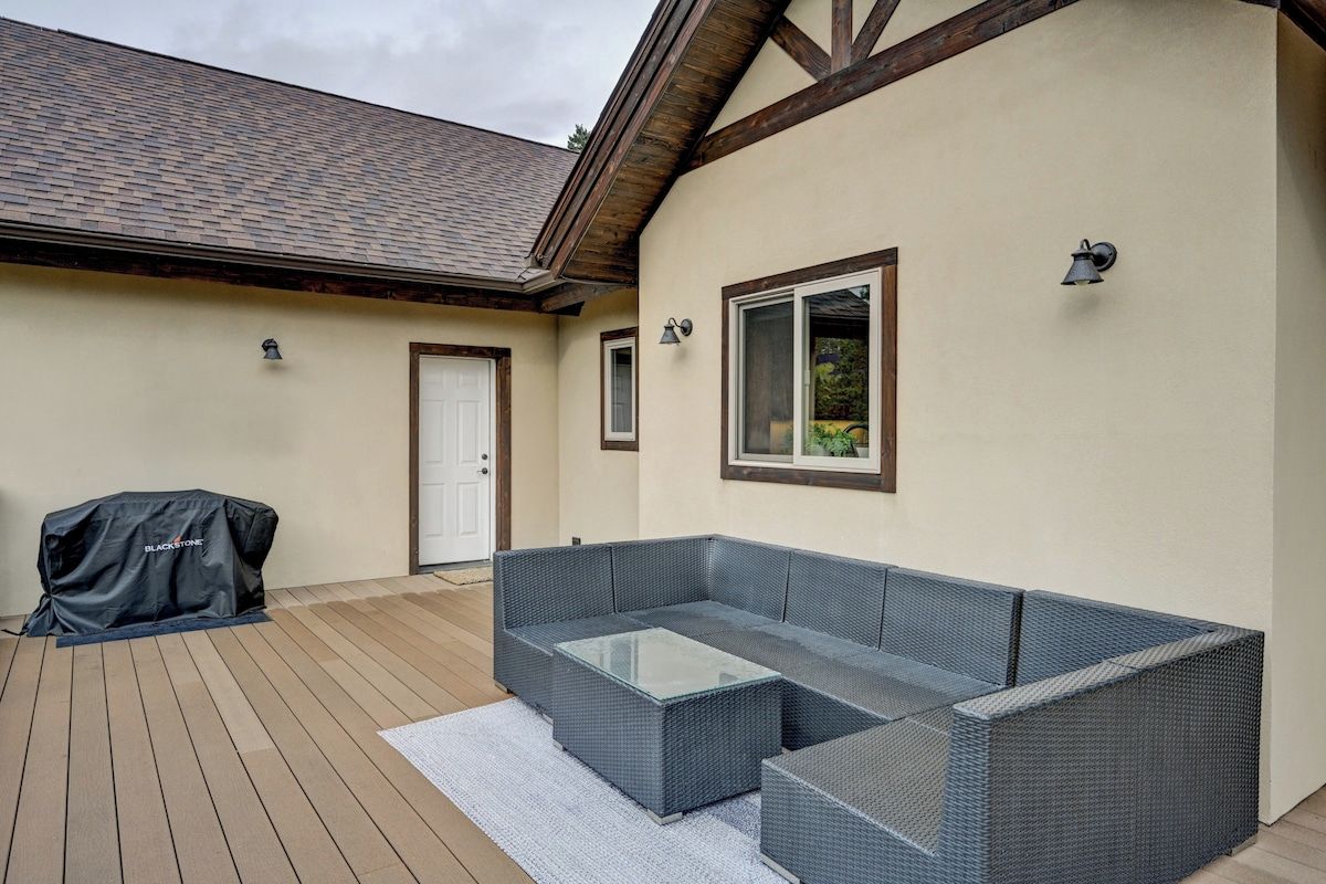 A covered outdoor seating area with a sofa and a glass-top coffee table, a barbecue grill, and a door leading to the house.