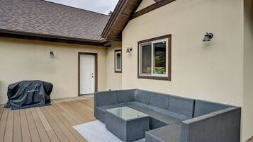 A covered outdoor seating area with a sofa and a glass-top coffee table, a barbecue grill, and a door leading to the house.