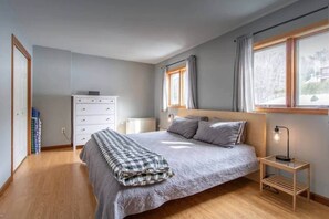 A bedroom with a bed, bedside tables, a dresser, and a window with curtains. - Burke Mountain Condo, Steps to Kingdom Trails (Burke)