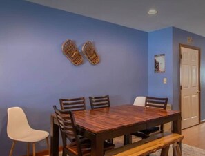 A dining area with a wooden table and chairs, a bench, and a wall-mounted shoe rack. - Burke Mountain Condo, Steps to Kingdom Trails (Burke)