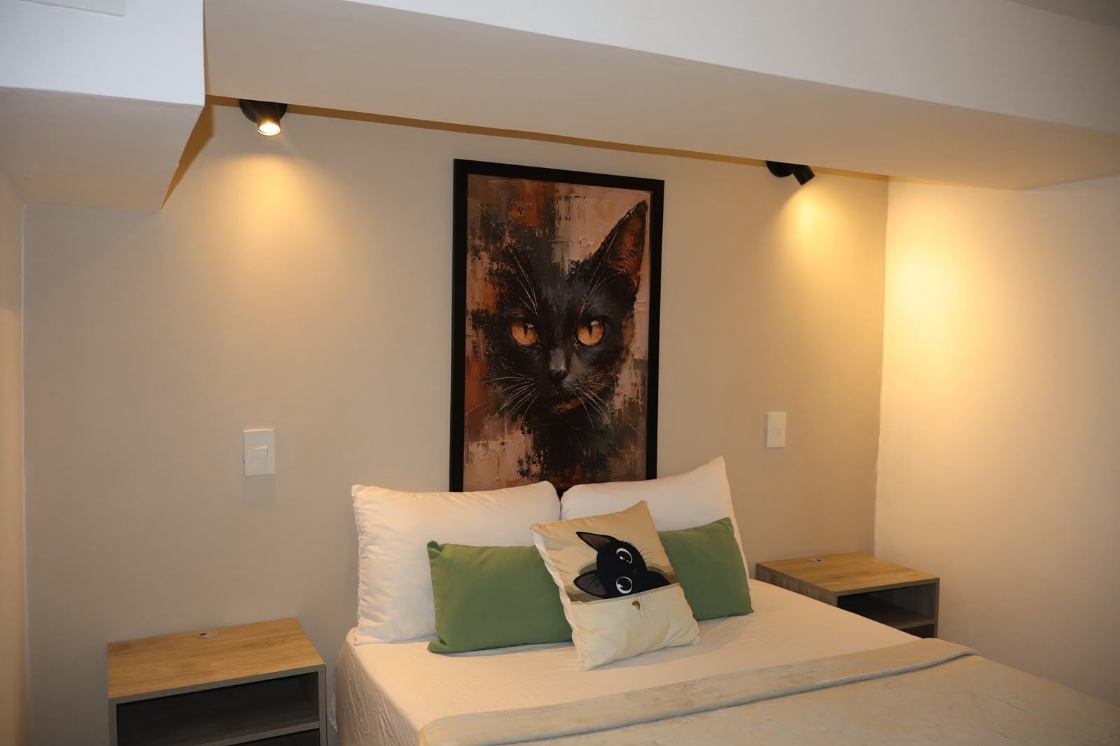 Un dormitorio con una cama grande, dos mesitas de noche y un cuadro de un gato colgado en la pared.