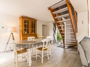 Un coin repas avec une table ronde et des chaises blanches, un buffet en bois et un escalier.