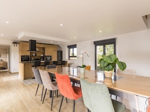A modern kitchen with wooden cabinets, a dining area with a large table and chairs, and a view of the outdoors through a window. - Quiet family house - flexible capacity (Saint-Jacques-de-Néhou)