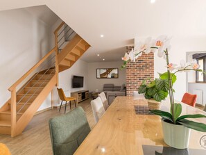 Ein moderner Wohnbereich mit einer Holztreppe, einem Essbereich mit einem Glastisch und einer Wand mit Backsteinverkleidung.