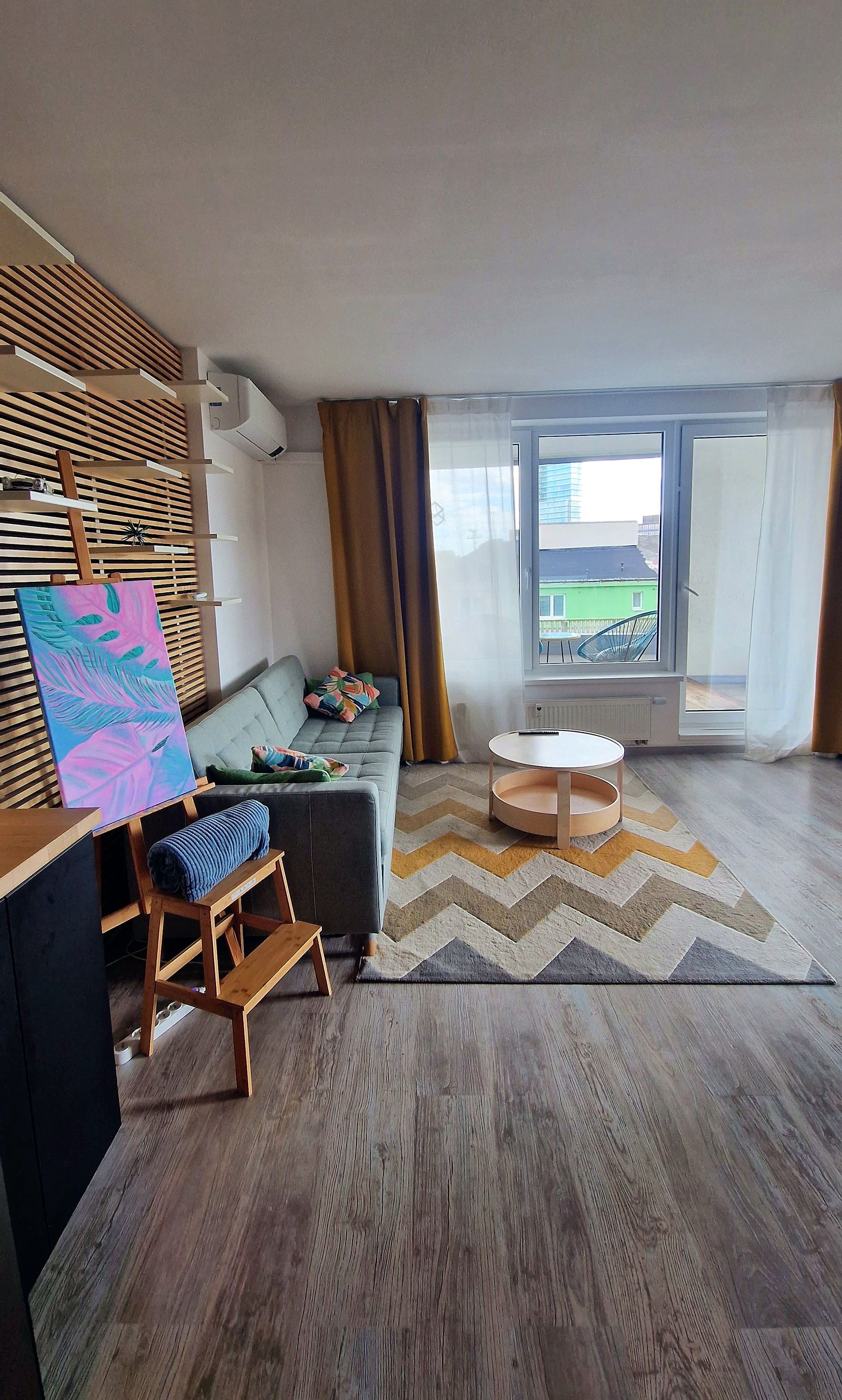 Un salon moderne avec un canapé gris, une table basse en bois et un tableau coloré accroché au mur.