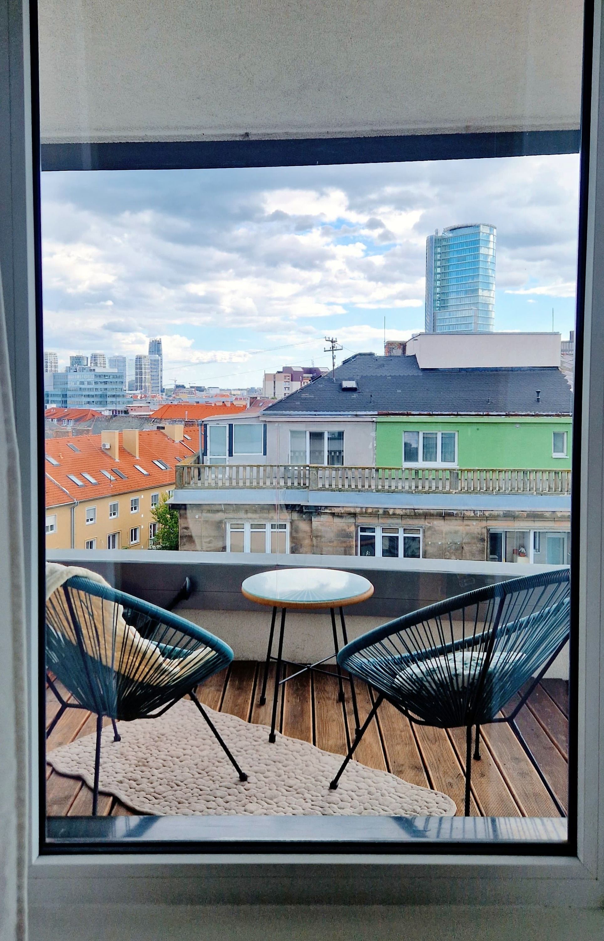 En balkon med to stole og et lille bord, med udsigt over bybilledet med forskellige bygninger.