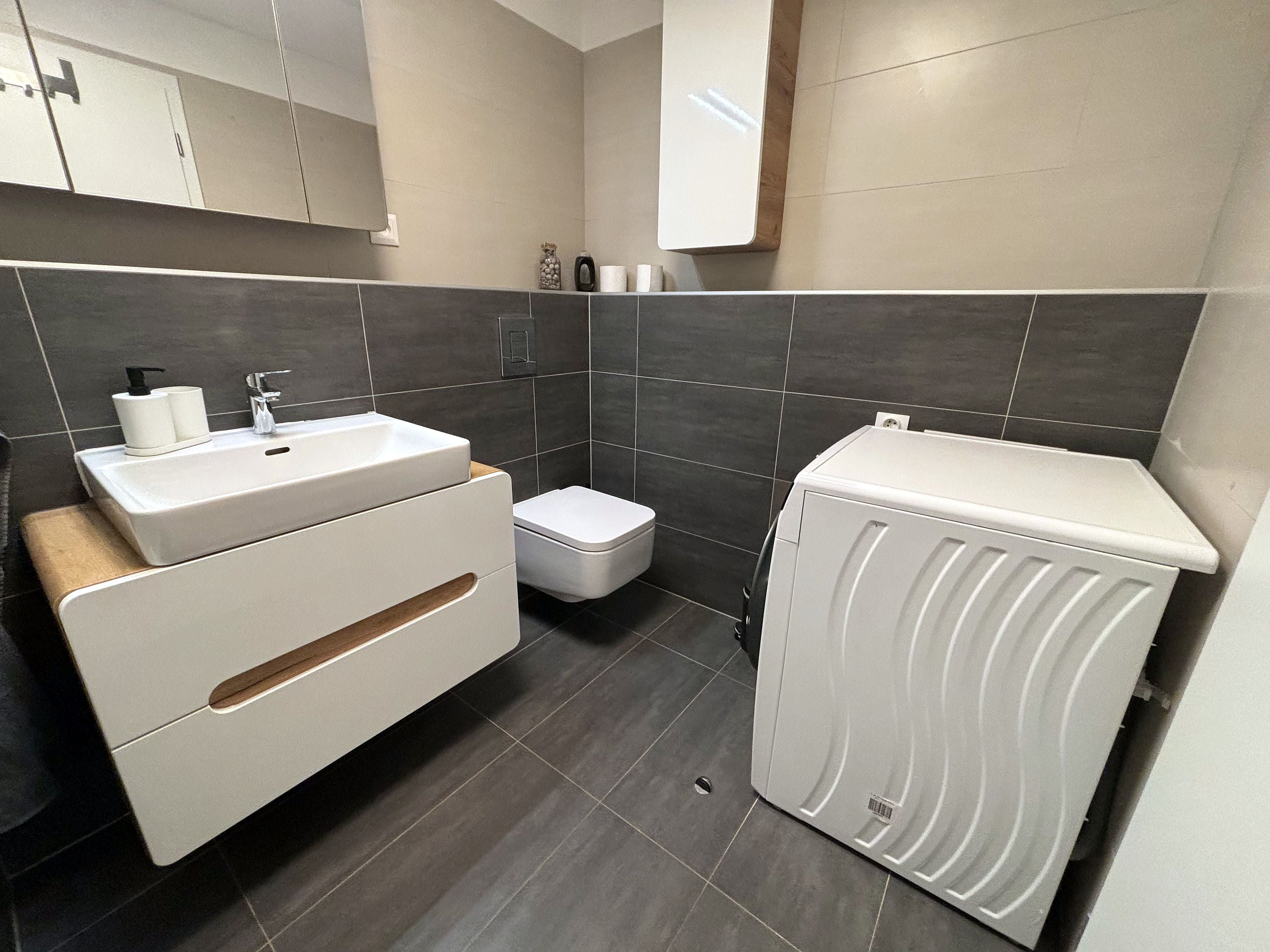 A modern bathroom with a white sink, toilet, and washing machine.
